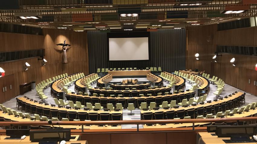 General view of the Trusteeship Council from the third floor, with chairs arranged around the room and a projector screen on the front wall of the chamber. 