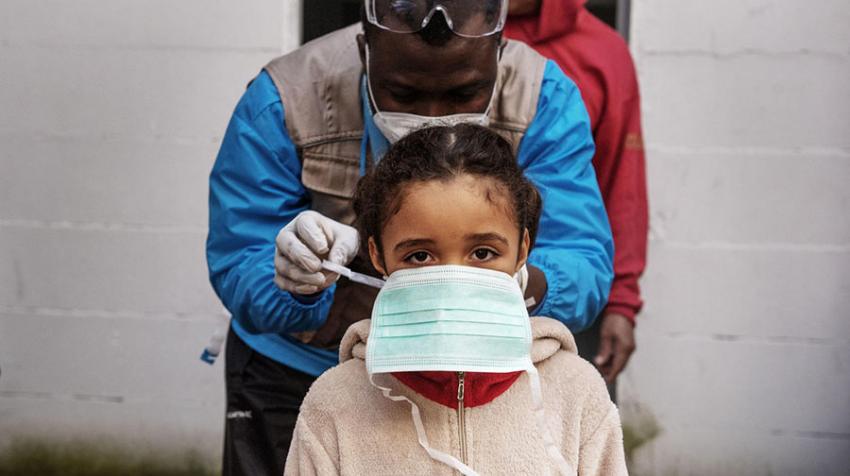 Un travailleur humanitaire de l'UNICEF aide une fille à attacher son masque. UNICEF/Alessio Romenzi