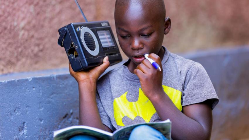 Boy holding a radio in one hand and a pencil in the other.