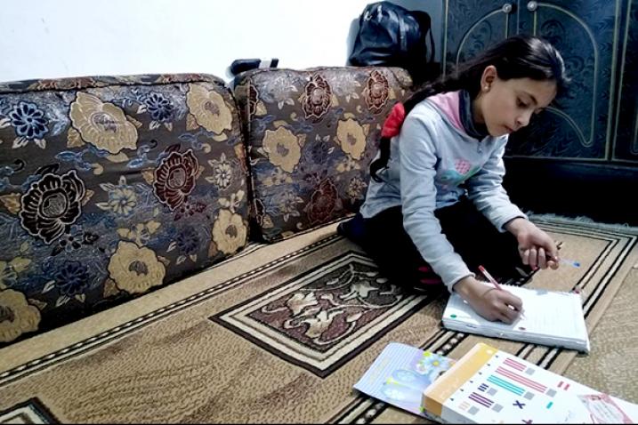 Una niña estudiando en el suelo de su habitación.