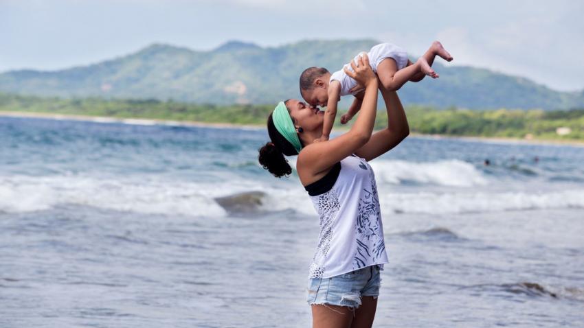 Una madre levanta a su bebé en brazos en una playa.