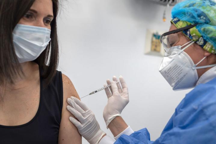 Una sanitaria poniendo la vacuna contra la COVID-19 a una mujer. Ambas llevan mascarilla.