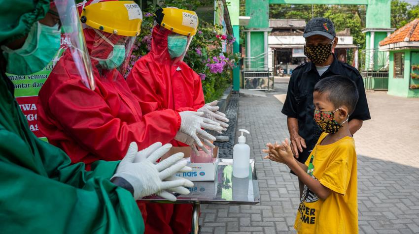 Health workers demonstrate proper handwashing to a child wearing a mask.