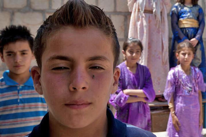 Four Iraqi children. A boy in the foreground. Another boy is at left. Two girls are at right.