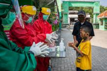 Health workers demonstrate proper handwashing to a child wearing a mask.