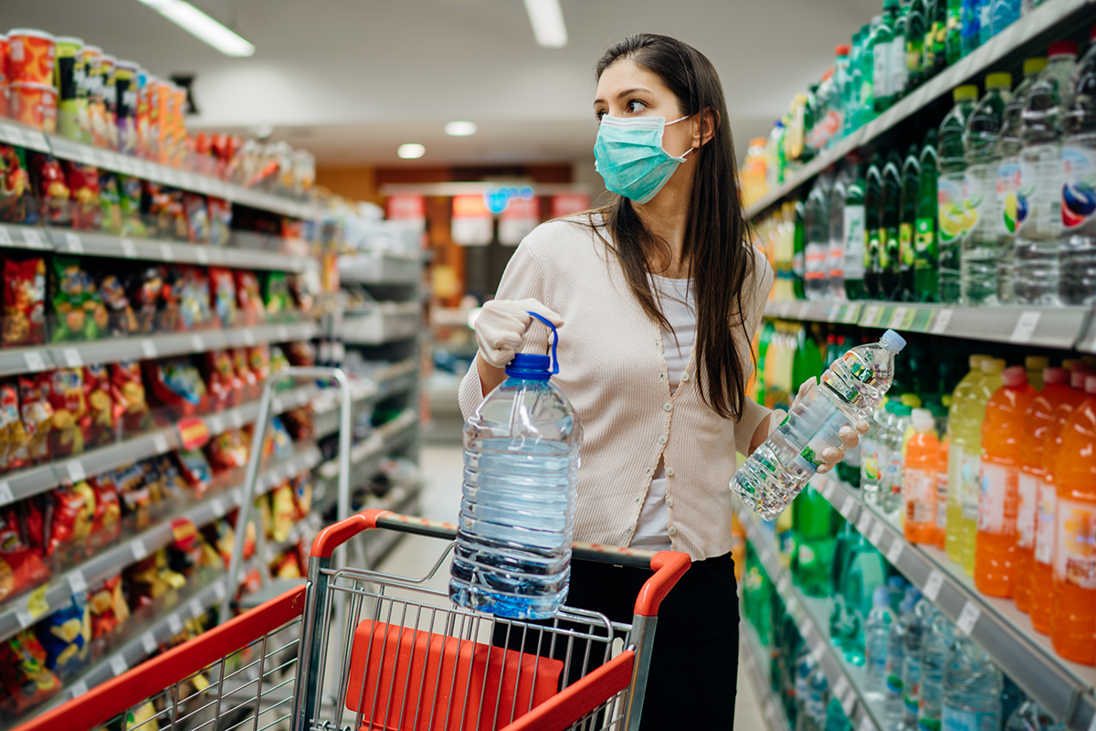 A woman wearing a facemask at a supermarket holds two bottles of water. 