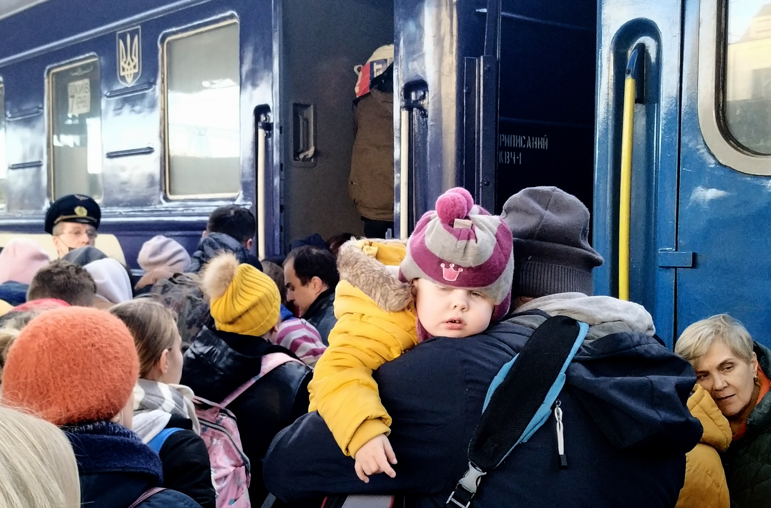A man holds a baby among a crowd boarding a train