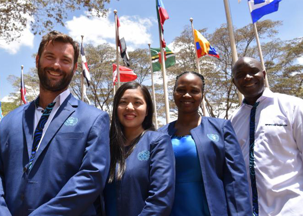 Four UN Tour Guides wearing United Nations Visitor Centre uniforms stand side by side, looking at the camera and smiling.