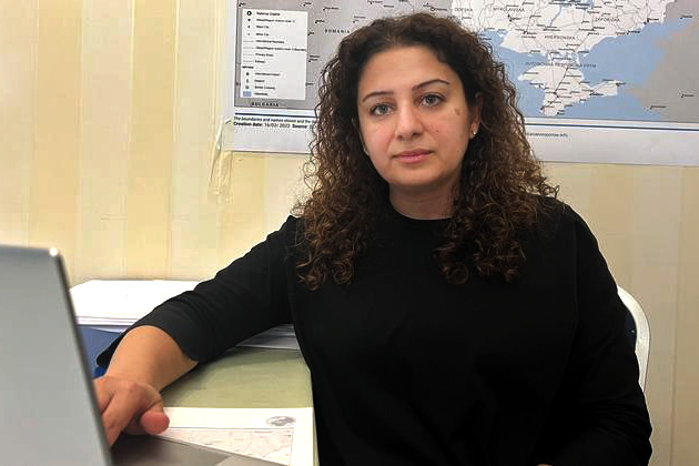 A woman sits in front of her computer with a map of Ukraine on the wall behind her