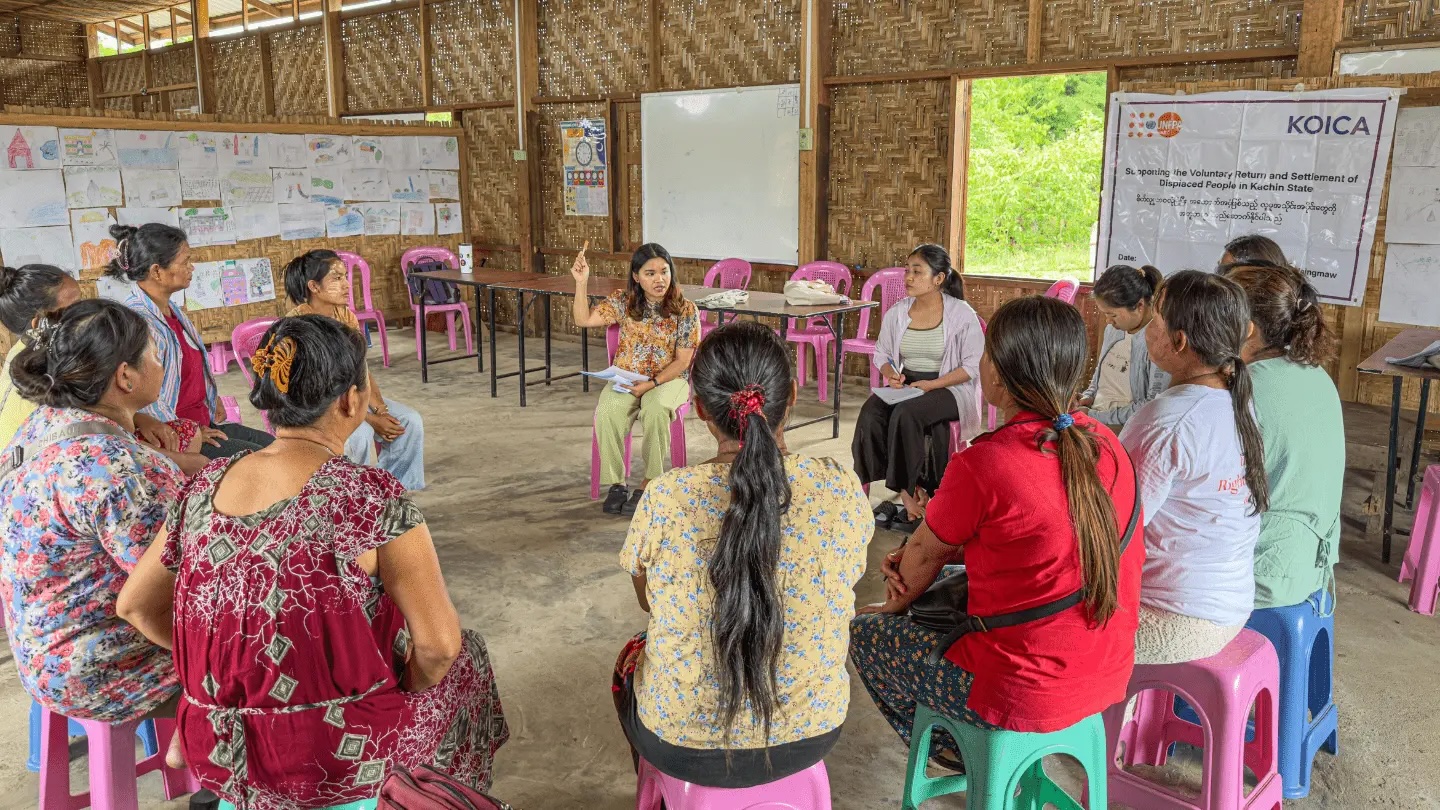 Women seated in a circle on colorful stools in a bamboo-walled classroom