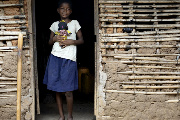 Girl holding a door at the entry of a mud hut.