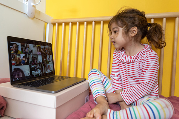 A little girl sits in front of a computer on a video chat. 