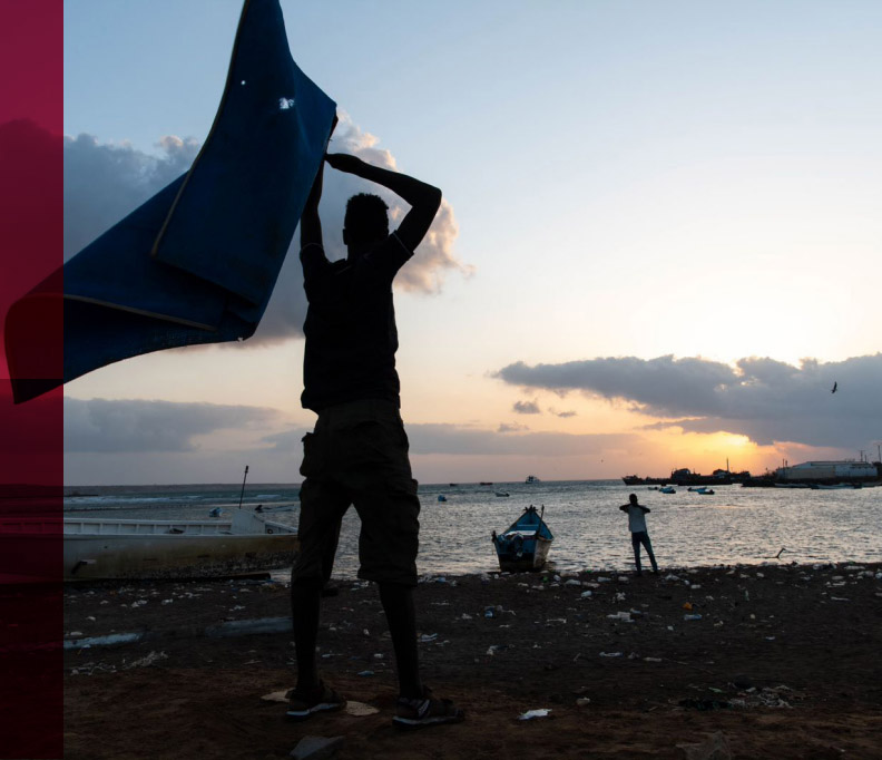 Foto de la portada del informe 'https://www.ilo.org/global/topics/forced-labour/publications/WCMS_854797/lang--es/index.htm', en la foto se ve la silueta de una personas de espaldas y dos en el fondo, en una playa.