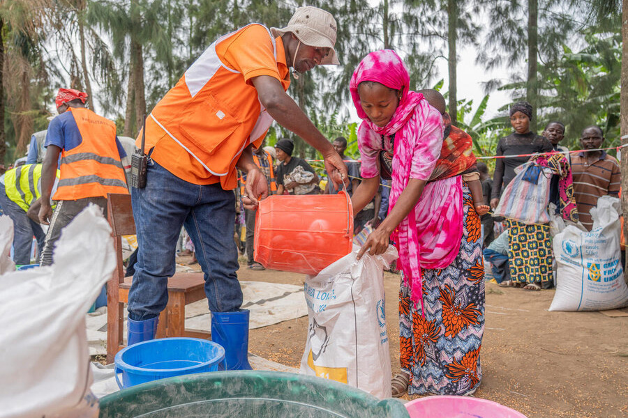 A humanitarian worker is filling out a bag of food for a young mother. WFP/Benjamin Anguandia