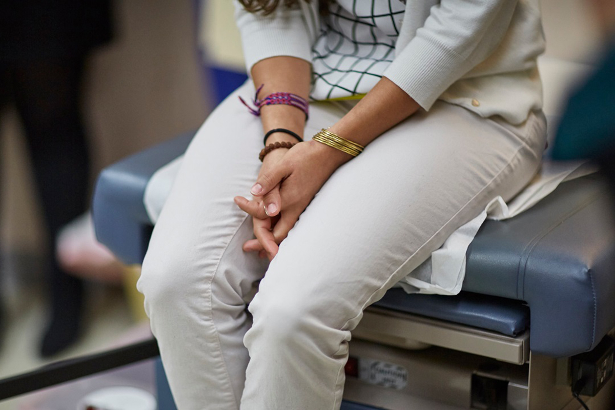 Photo of a woman, waist down, sitting at a doctor’s chair. 