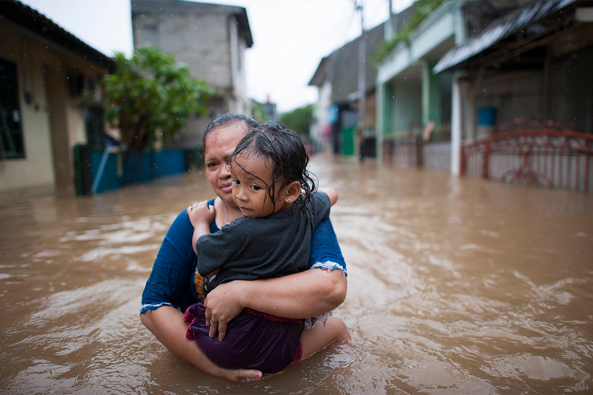 A woman holds a girl while walking in a hips-height flooded street