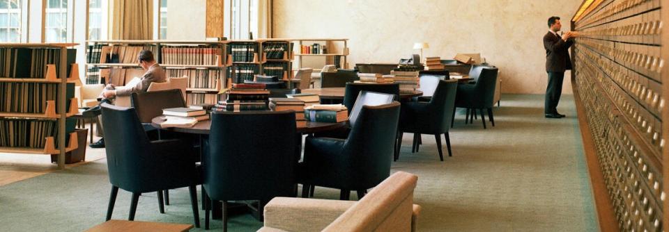 Two men at opposite corners of a library reading books