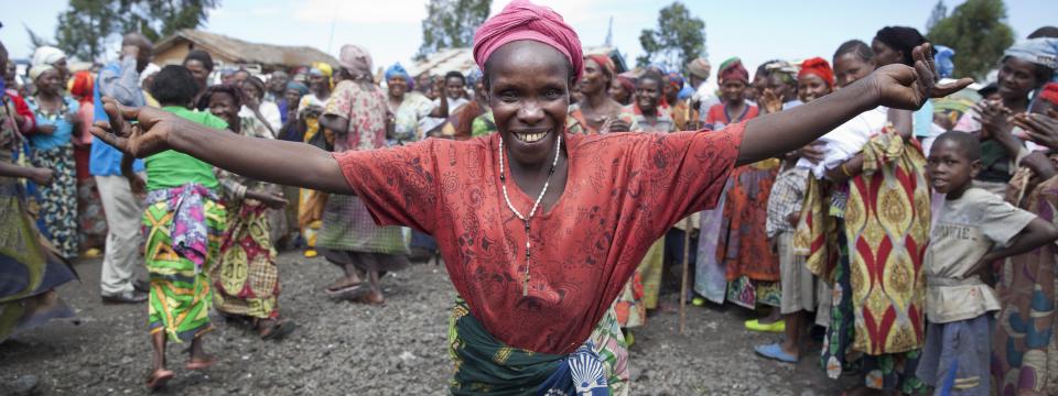 Happy elderly woman warmly welcoming UN staff to the community with open arms and a smile.