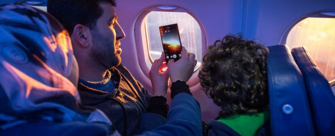 Una familia mira por la ventana del avión y toma fotos mientras viajan a su nuevo hogar. Foto: OIM / Muse Mohammed