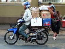 A motorcycle 'taxi' driver transports a trader and dry goods to the Phnom Penh market, Cambodia.