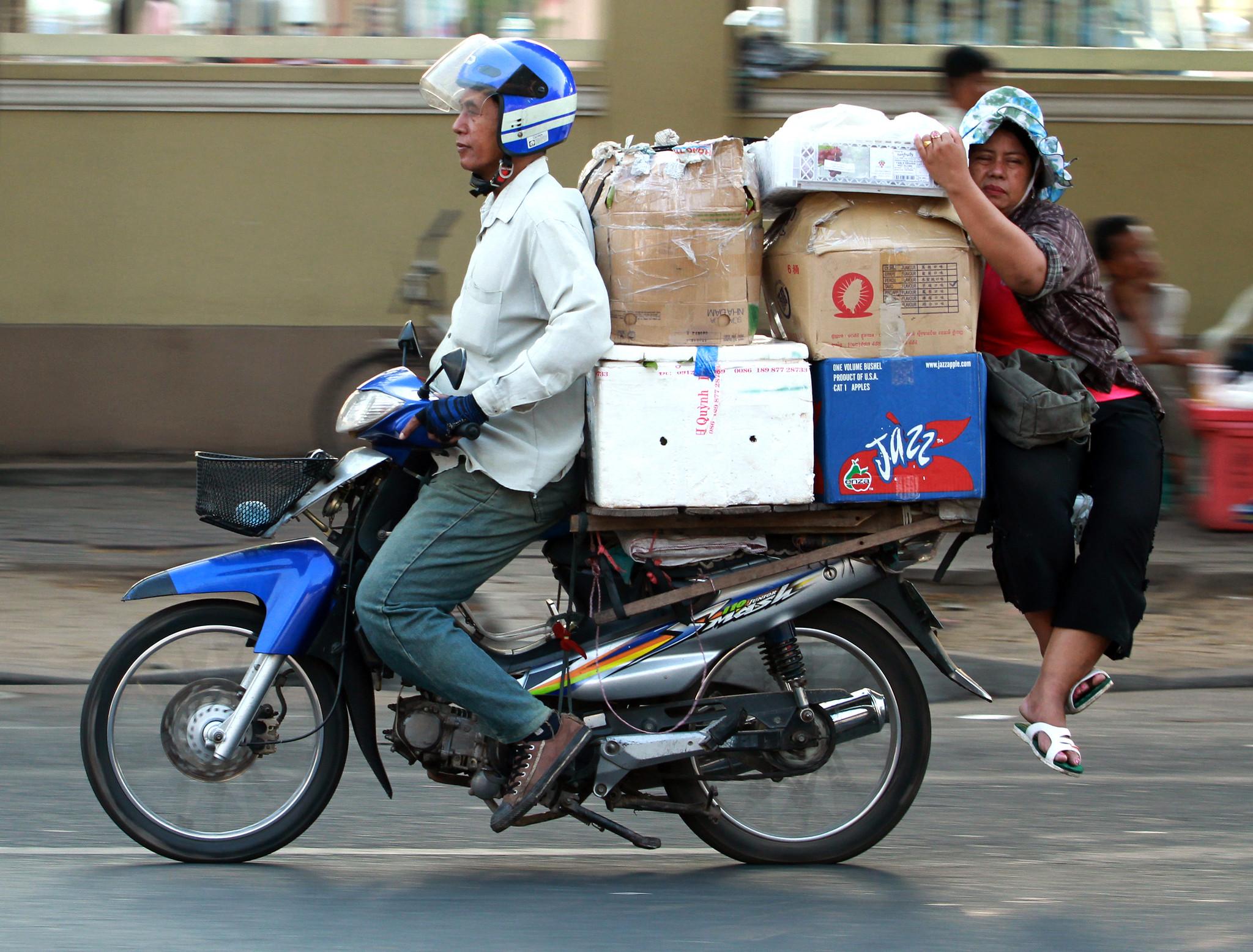 A motorcycle 'taxi' driver transports a trader and dry goods to the Phnom Penh market, Cambodia.